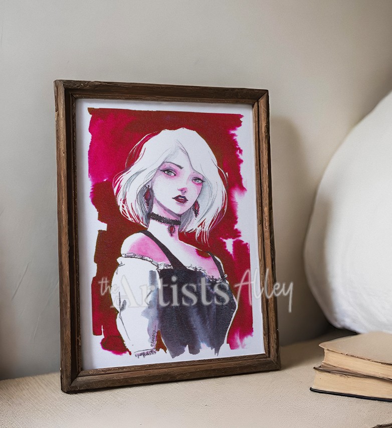 mise-en-scene-aquarelle-gothique-cadre-rustique-cozy-deco.jpg Photomontage d'une œuvre d'art encadrée posée sur une table de nuit ou un bureau en bois clair. Le cadre est rustique, patiné et de couleur marron foncé. À l'intérieur, l'aquarelle originale "La Dame de Sang" avec ses cheveux d'argent, son corset noir et son fond rouge vif est visible. L'arrière-plan montre une literie blanche texturée (lit ou canapé), un mur uni et une petite pile de livres anciens, créant une ambiance de chambre intime, littéraire et cosy-gothique. Idée de décoration murale pour fan de fantasy et de romantasy.